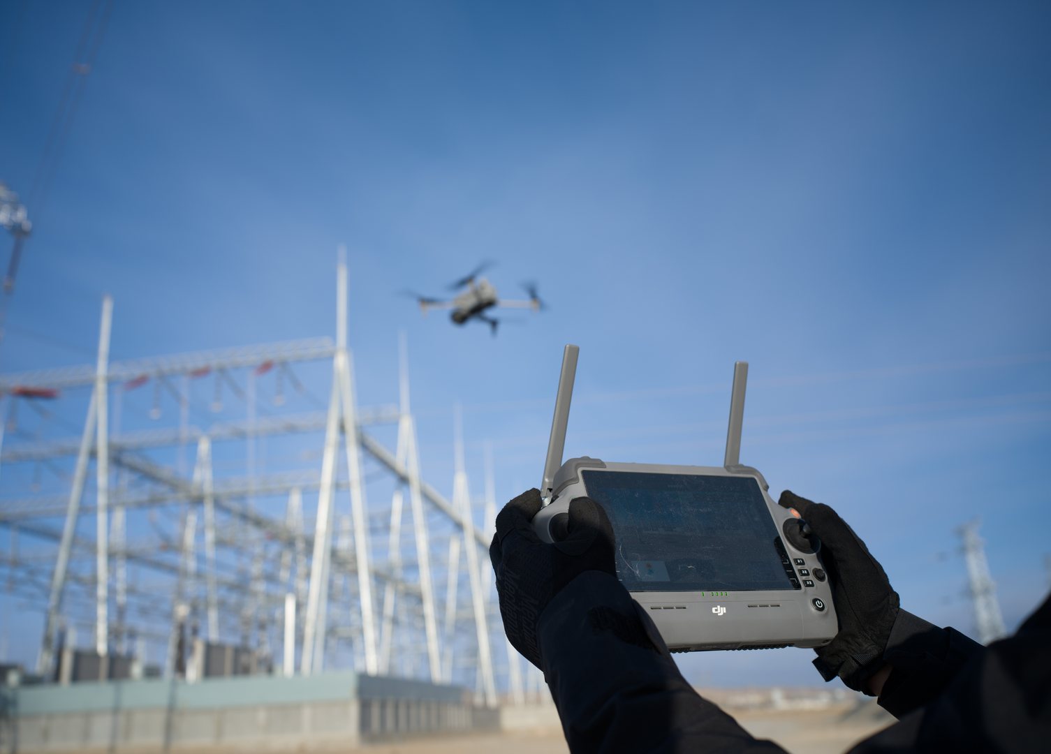 Opérateur pilotant le DJI Matrice 4T à la radiocommande lors d'une inspection de réseau électrique.